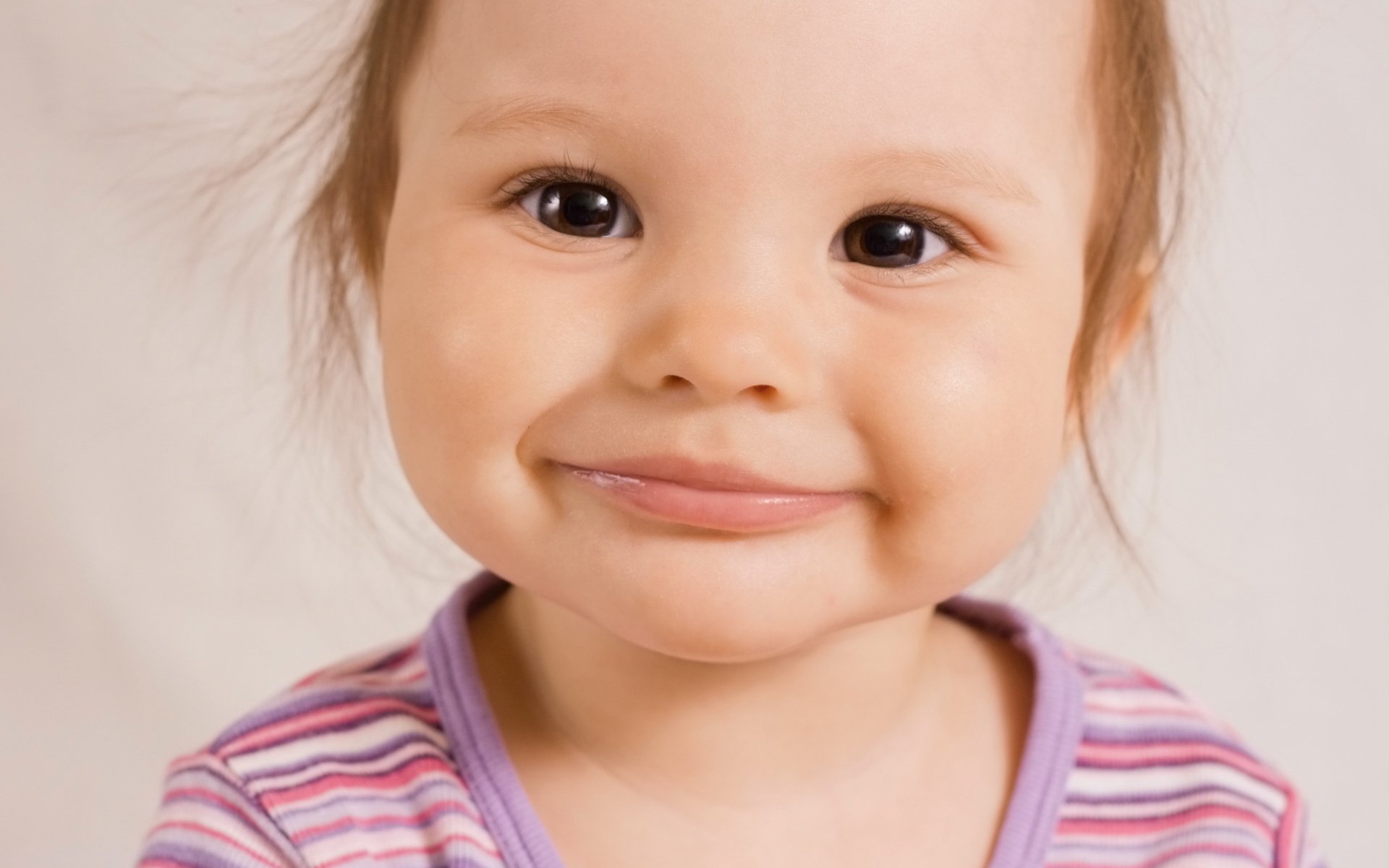 Кареглазая улыбающаяся маленькая девочка в полосатой футболке