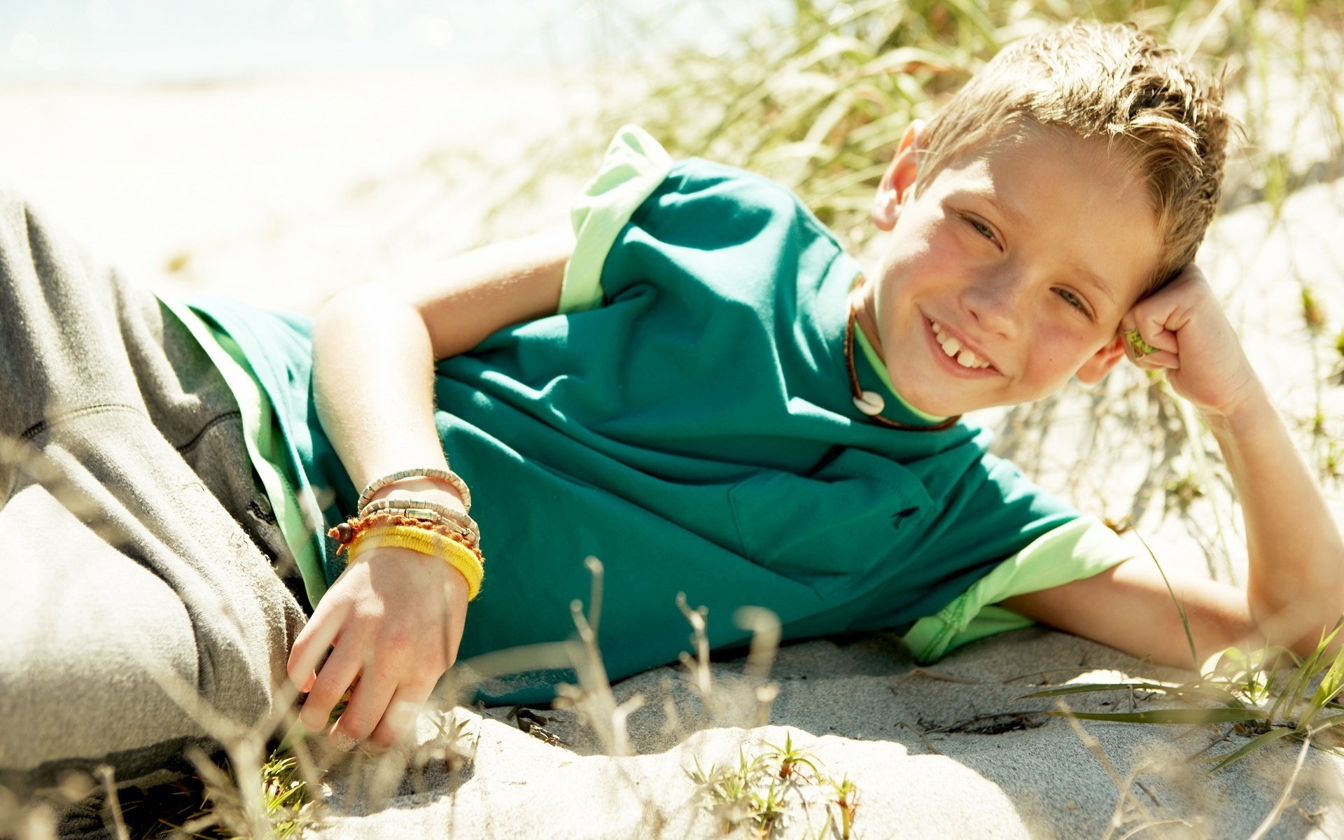 Мальчик лежит на песке и улыбается 