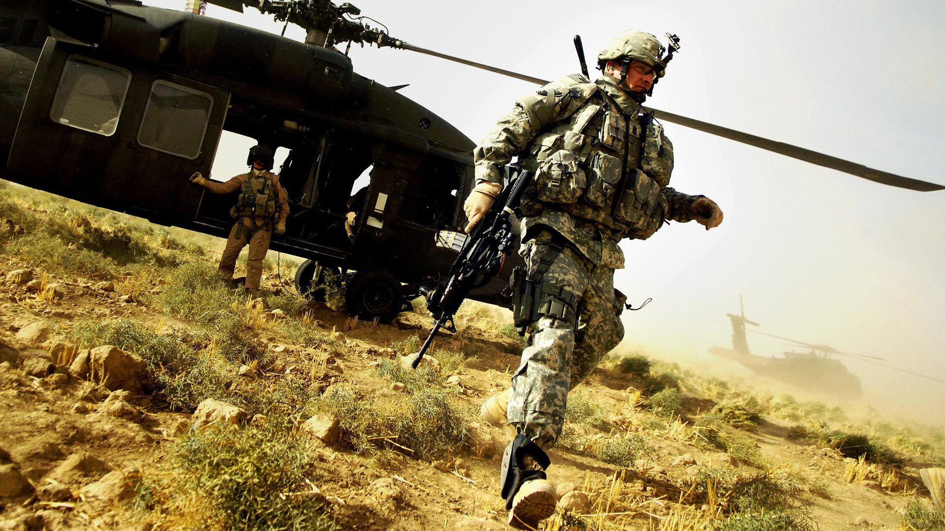 Военный человек с автоматом на фоне вертолета посреди поля
