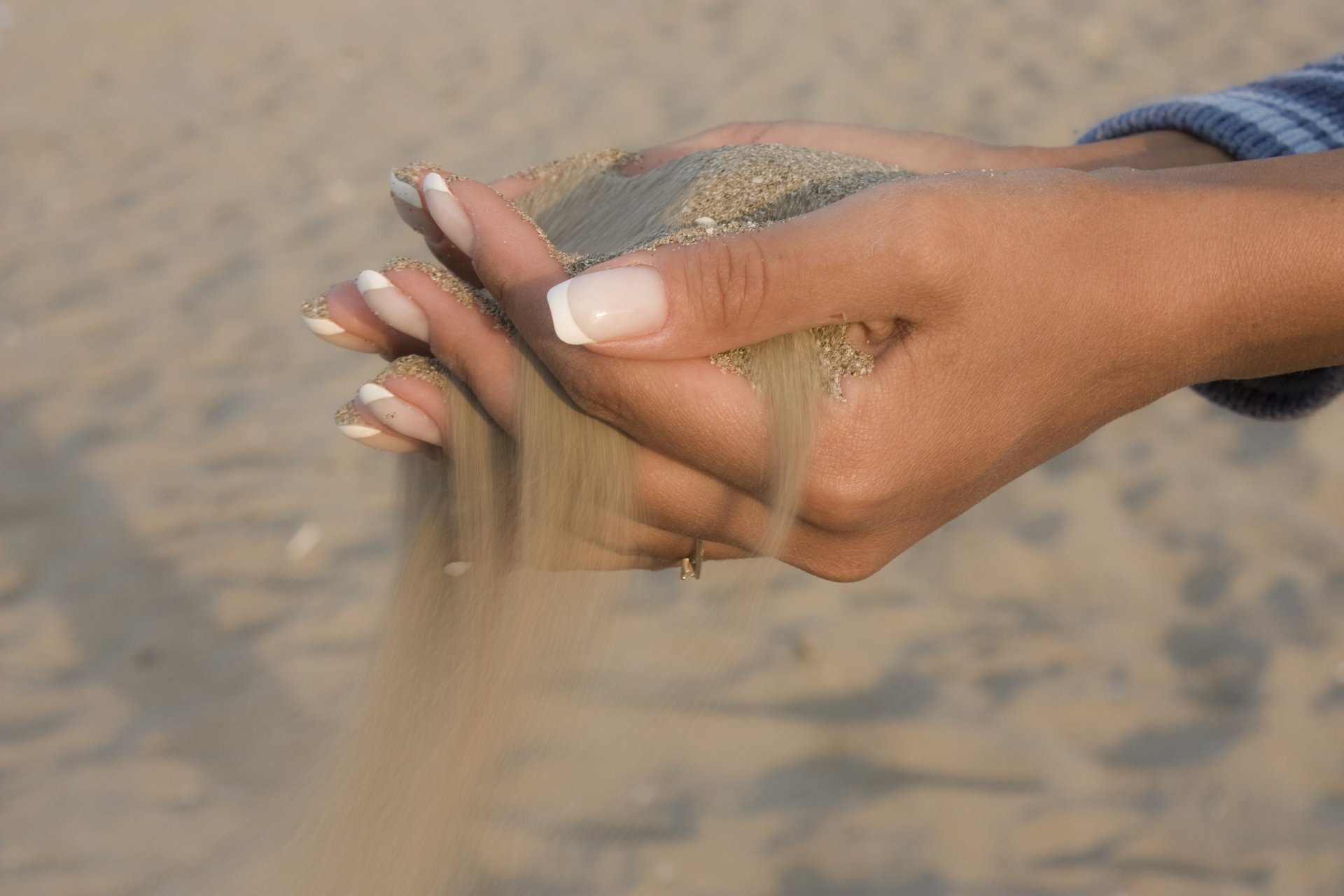 Пляжный песок струящийся сквозь женские пальцы