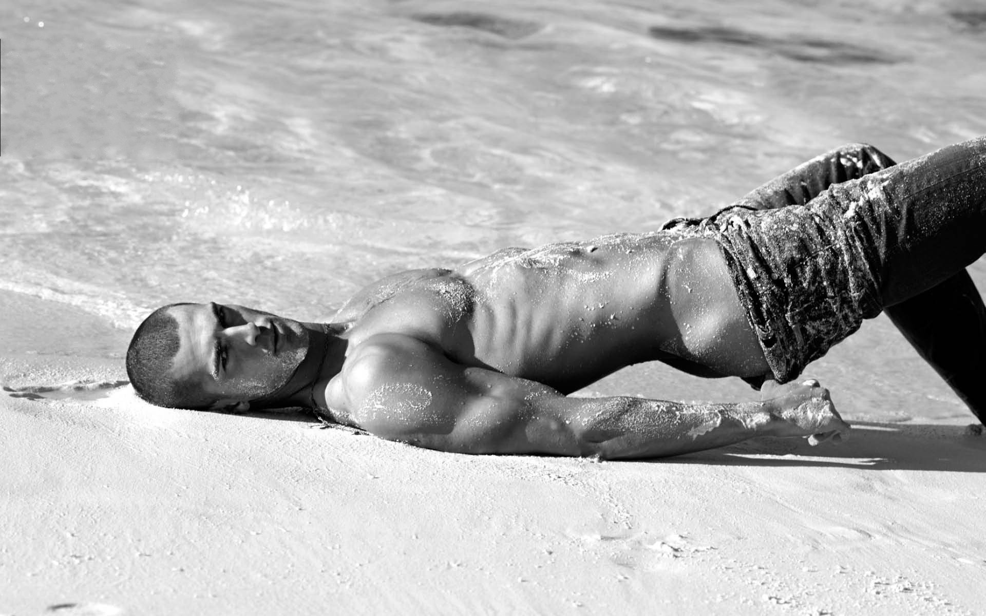 Чернобелая фотография красивого мускулистого парня в эротичной позе на песке