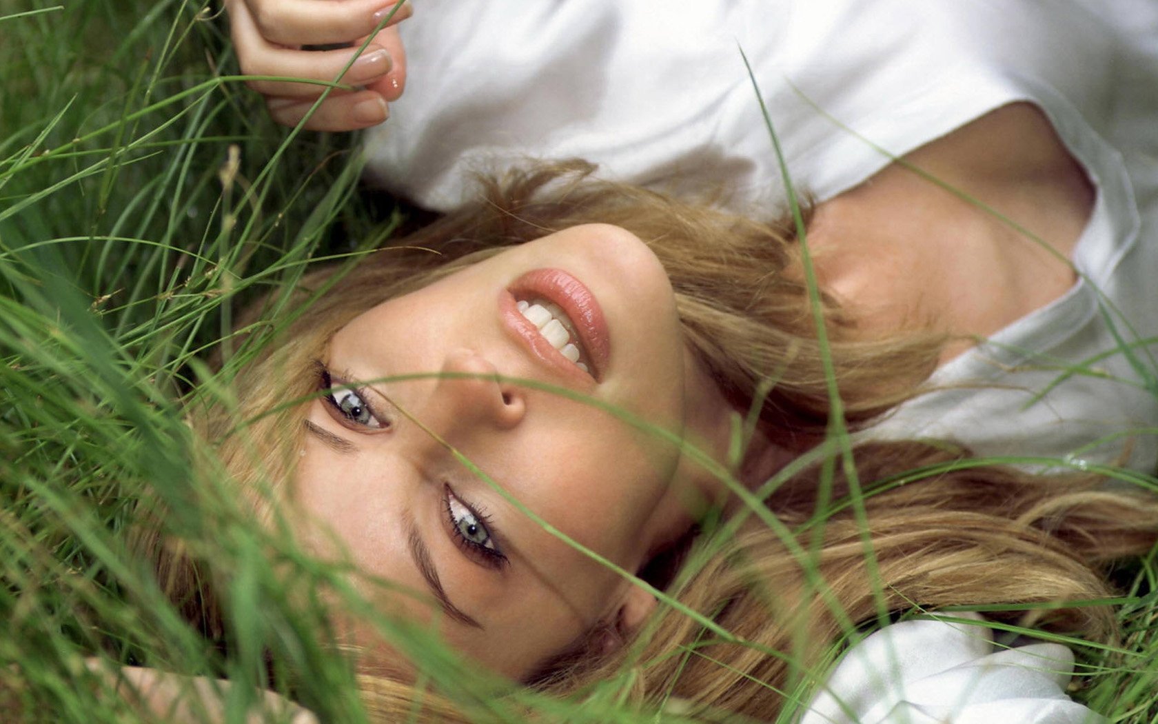 Светловолосая девушка сексуально улыбается лёжа в траве