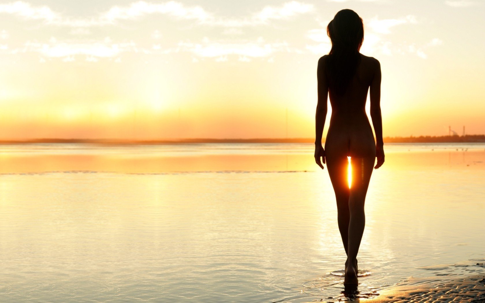 Силуэт обнаженной женщины на фоне заходящего солнца. Берег моря