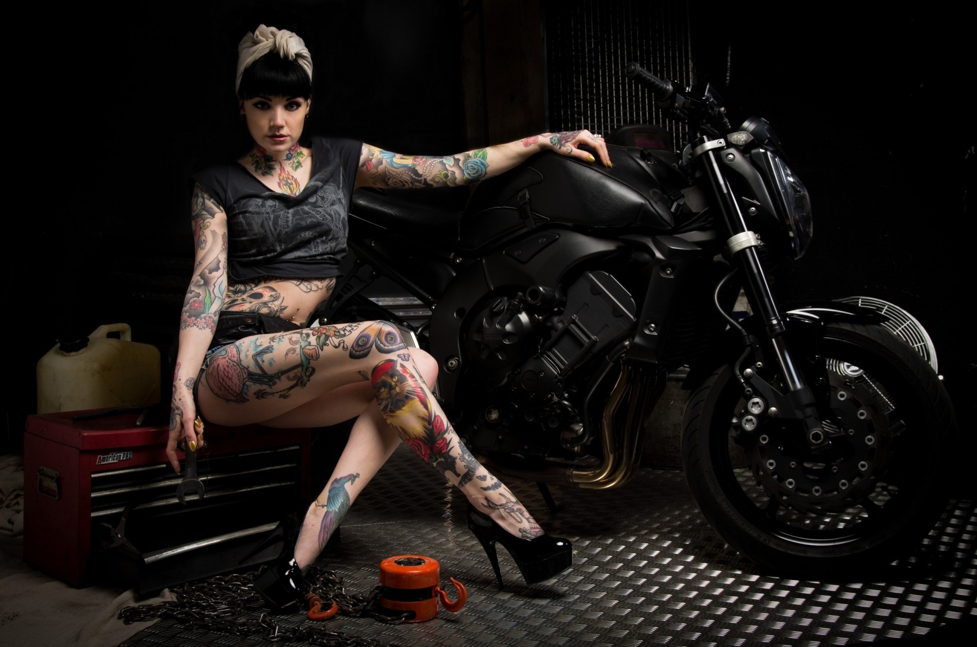 Девушка с татуировками сидит возле черного мотоцикла Обои на рабочий стол.