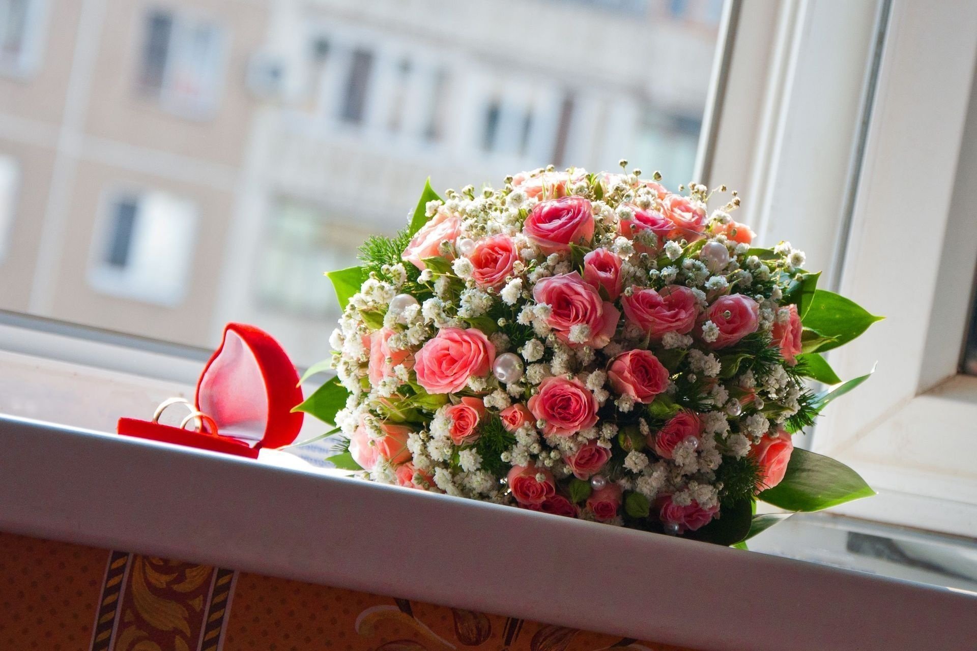 Свадебный букет роз и обручальные кольца в коробочке на подоконнике