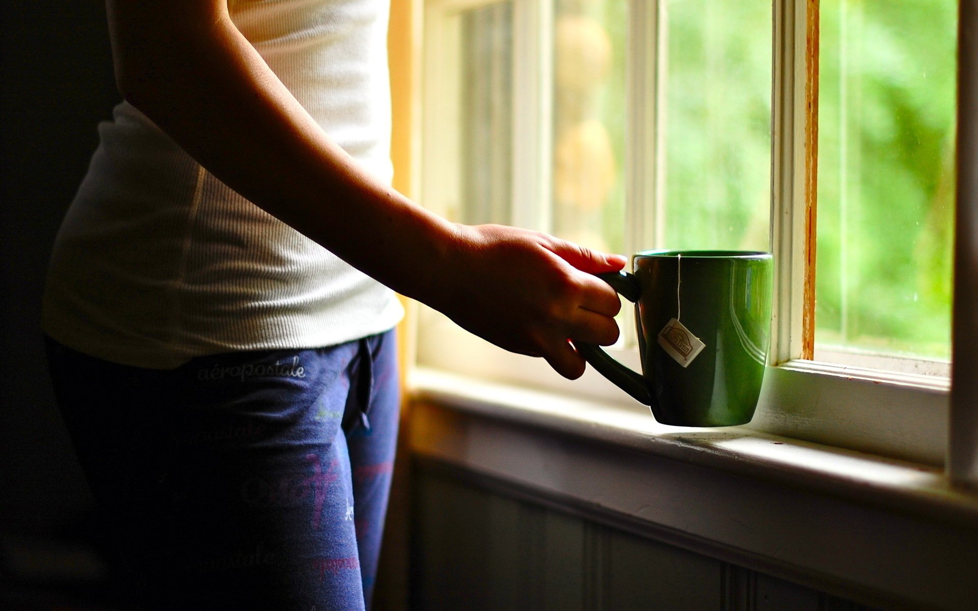 Зеленая чашка чая в руках у окна