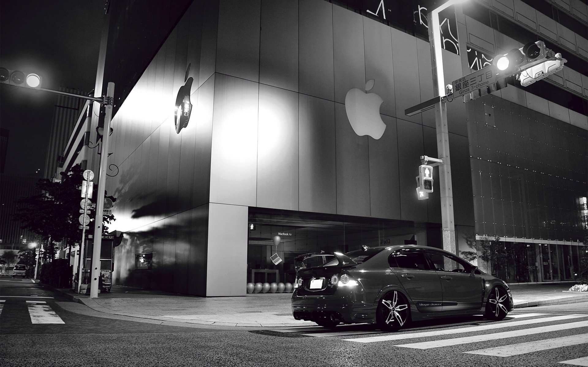 Чёрное-белое фото машины рядом со здание apple