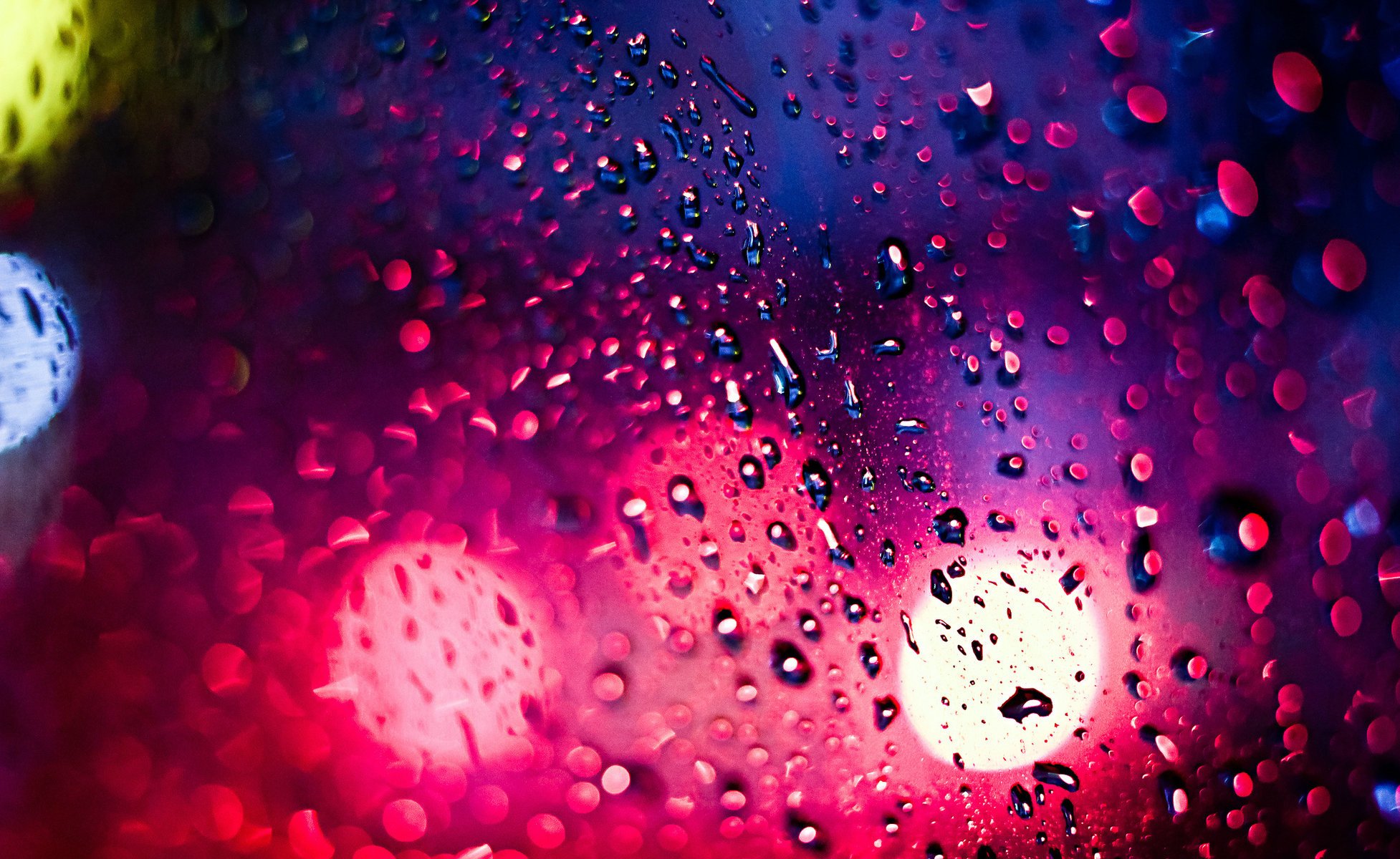 Городские разноцветные огни видны через абрызганное дождём стекло