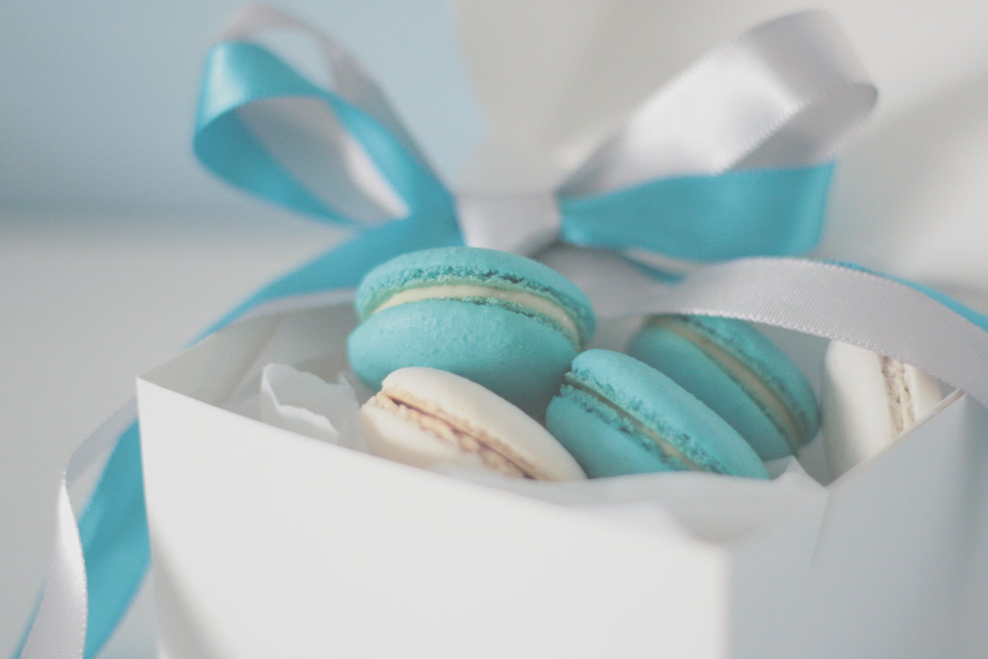 Голубое и белое печенье в белой коробке с голубой и белой ленточкаи на белом фоне