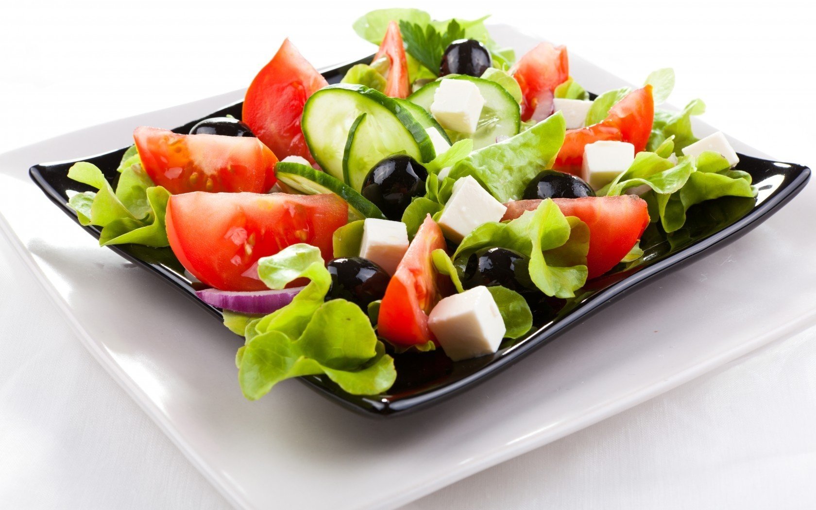 Греческий салат в чёрной тарелке на белой тарелке