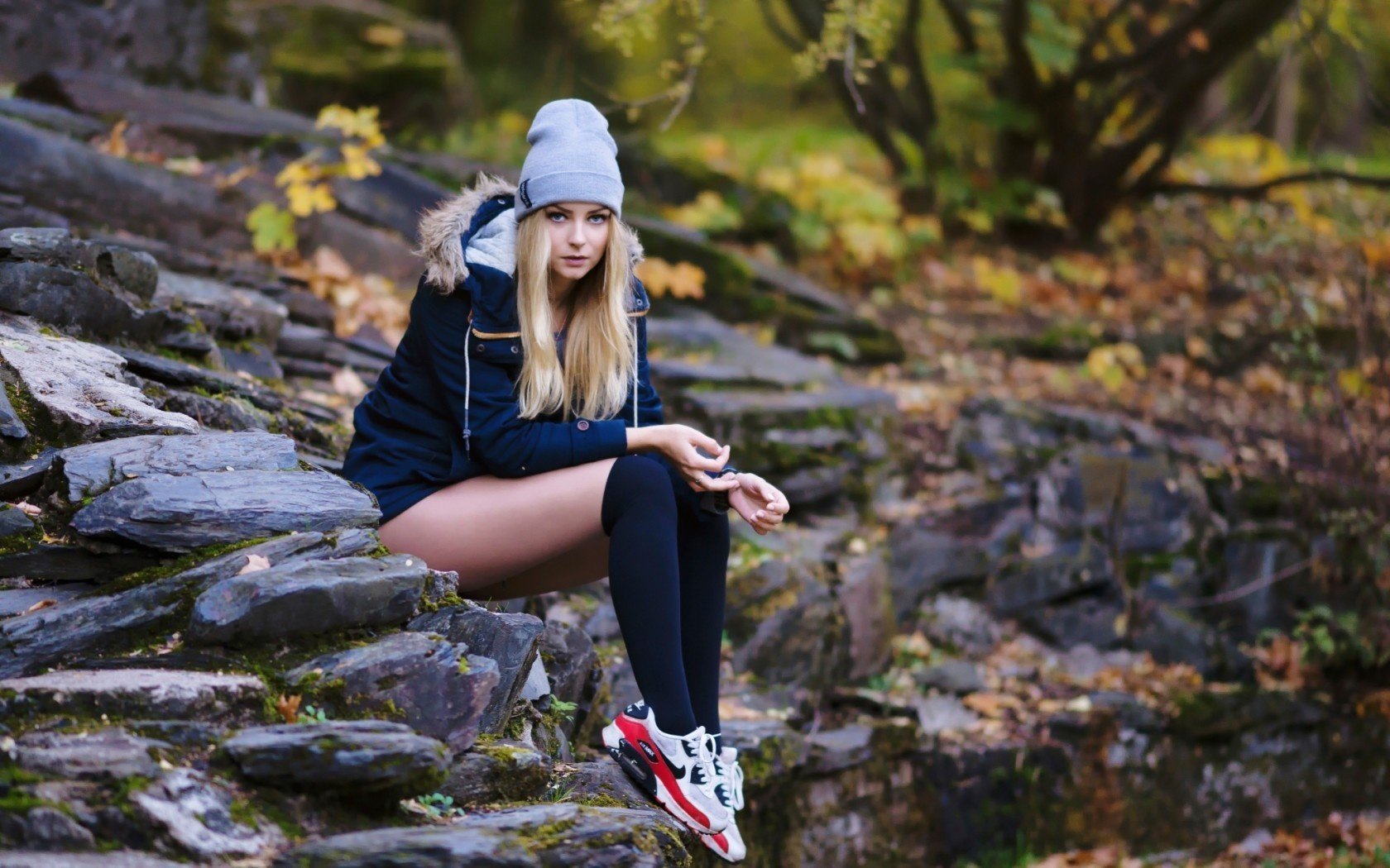 Девушка осенью со стройными ножками сидит на камнях