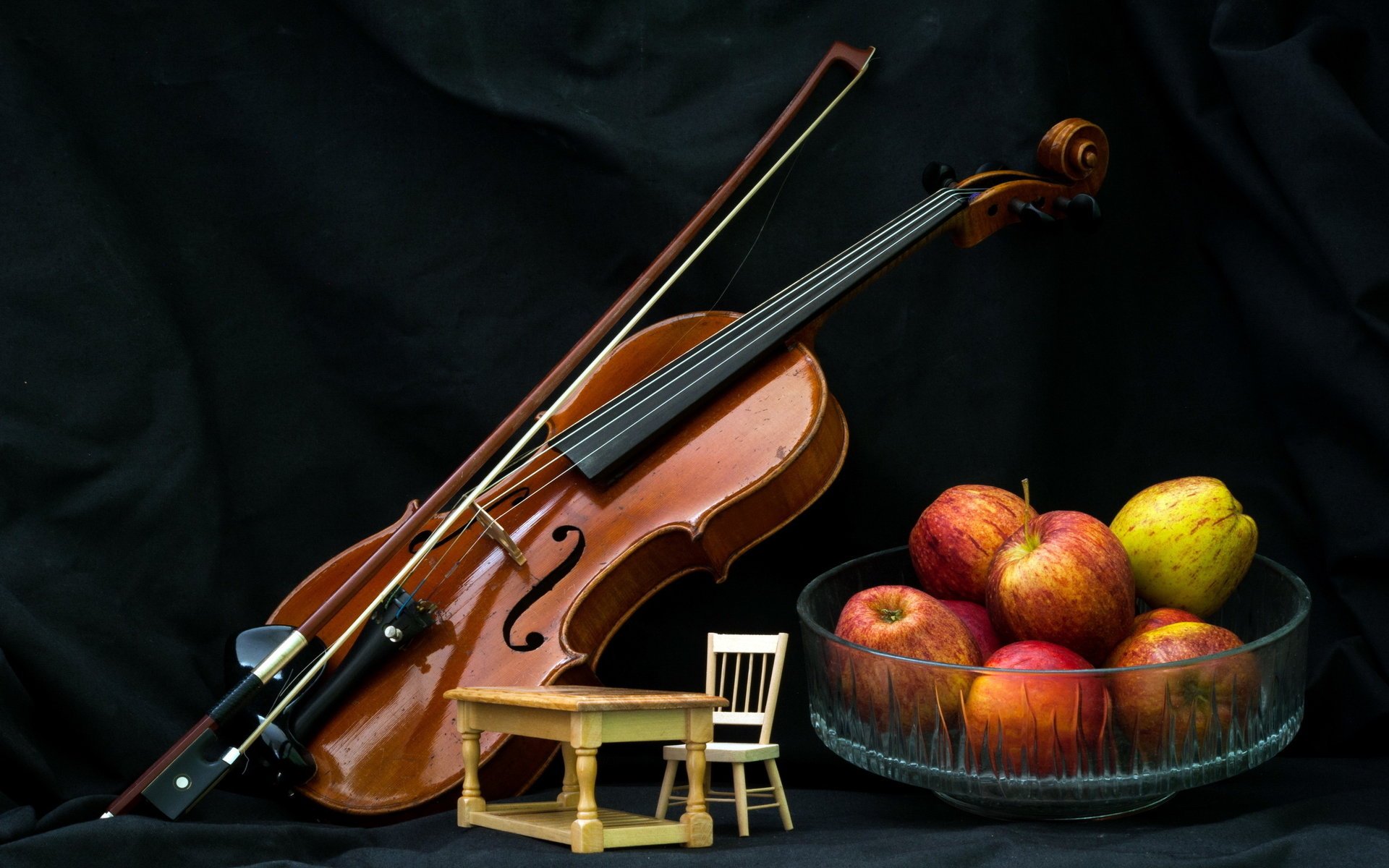 Скрипка, яблоки, стол со стулом на чёрном фоне
