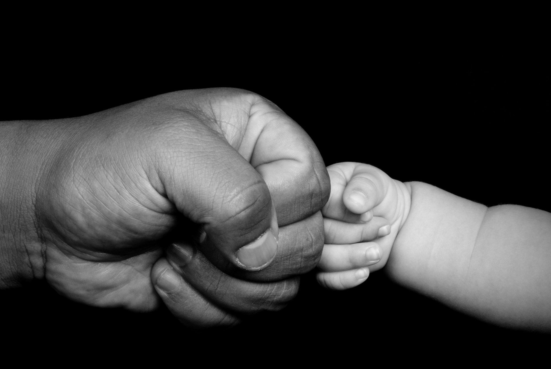 Рука мужчины и младенца на чёрном фоне