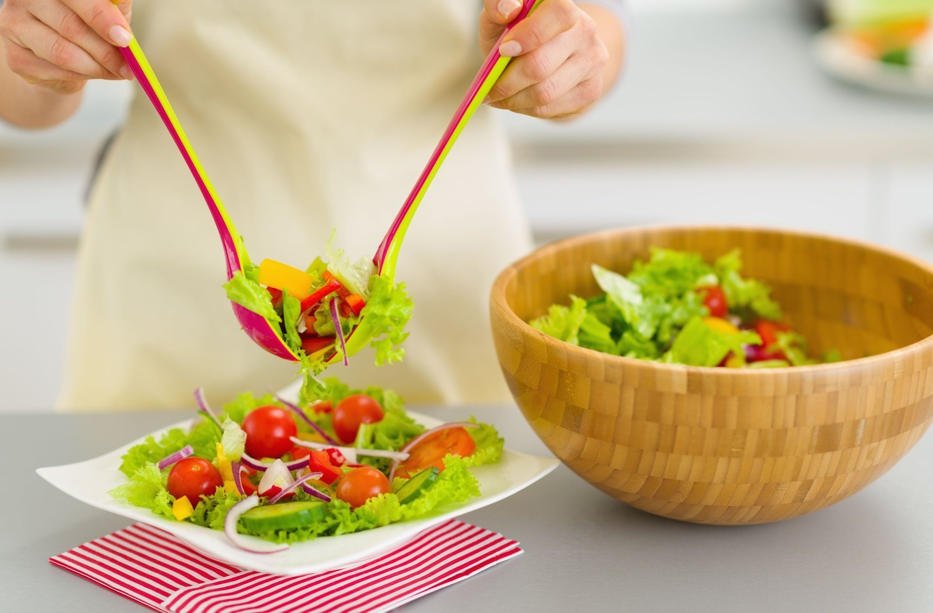 Руки накладывают зелёный салат в тарелку