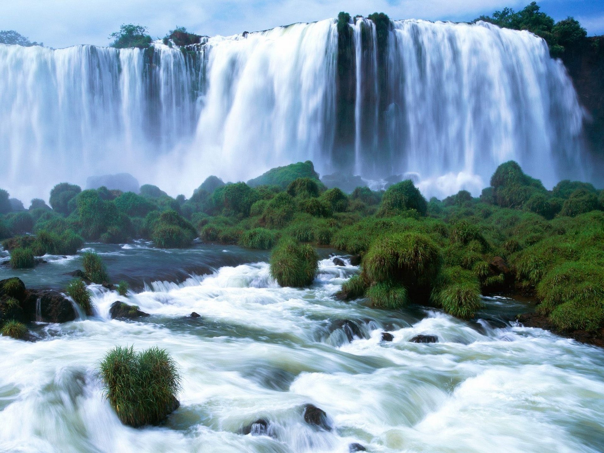 Бурный водопад, переходящий в реку, среди зелени