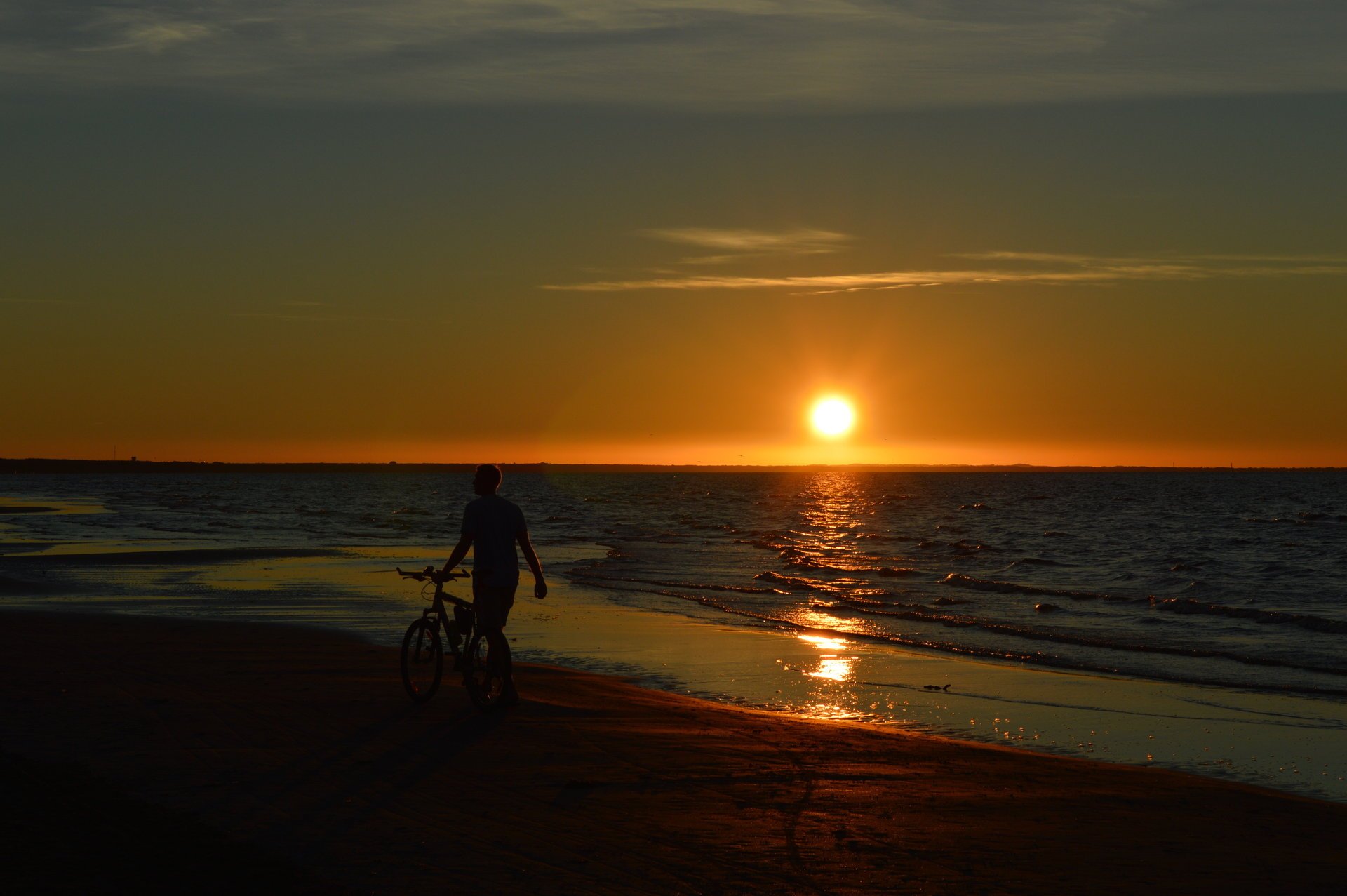 Человек бредущий по пляжу на фоне заката
