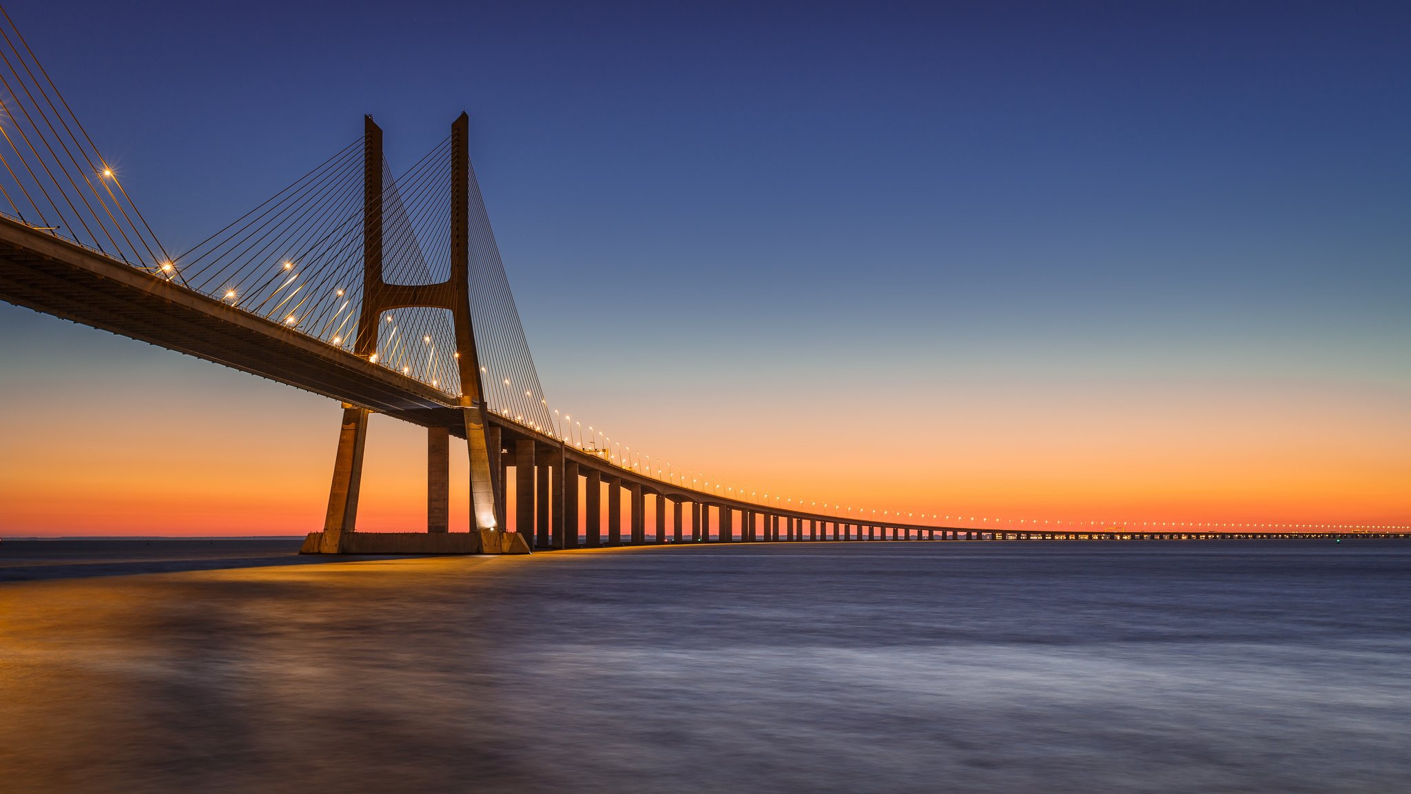 португалия лиссабон река тахо тежу мост васко да гама фонари освещение вечер оранжевый закат синее небо